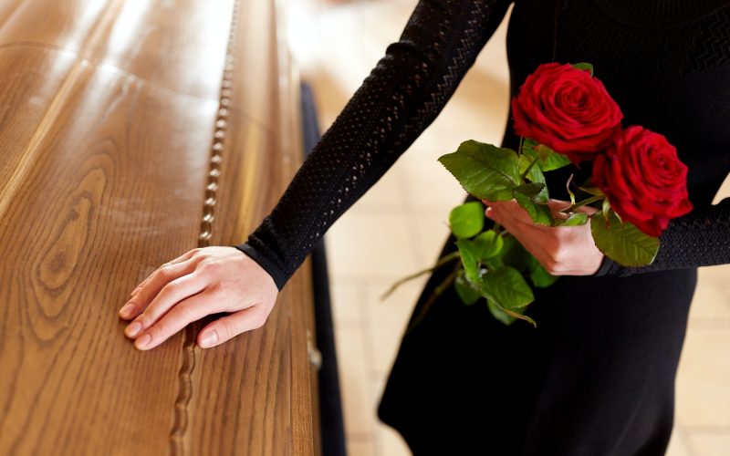 Mujer sujetando unas rosas al lado de un ataúd